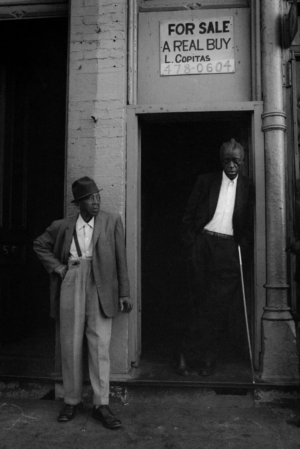 In my early photography days, I captured a unique moment on the west side of Chicago. Two men, one with a coat pulled back and the other blind, stood beneath a 'for sale' sign. It told a compelling story.